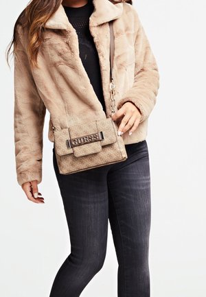 Beige faux bontjas met een brede kraag, gecombineerd met een tan handtas met patroon en een zilveren sluiting, gedragen met donkere spijkerbroeken.