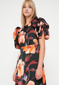 Φλοράλ φόρεμα σε μαύρο χρώμα με έντονα πορτοκαλί και μπλε λουλούδια. Διαθέτει φουσκωτά μανίκια και σχέδιο ελαστικής μέσης. Μια απαλή υφή υφάσματος.