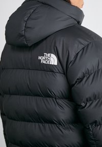 Giacca a vento nera con cappuccio, design trapuntato e logo "THE NORTH FACE" in bianco sul retro. Tessuto liscio e isolato.