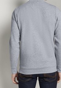 Sudadera gris con mangas largas y puños acanalados, hecha de una tela suave. Diseño liso, con un escote redondo y un corte relajado.