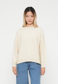 Maglione oversize beige chiaro realizzato in tessuto morbido, con scollatura rotonda e orlo a costine. Abbinato a jeans in denim a gamba larga.