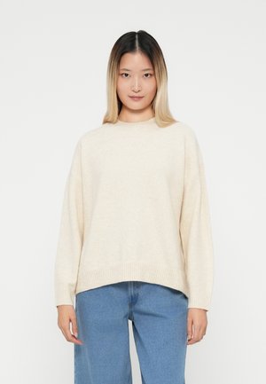 Jasno beżowy oversize sweter wykonany z miękkiego materiału, z okrągłym dekoltem i ściągaczem u dołu. W zestawie z szerokimi dżinsami.