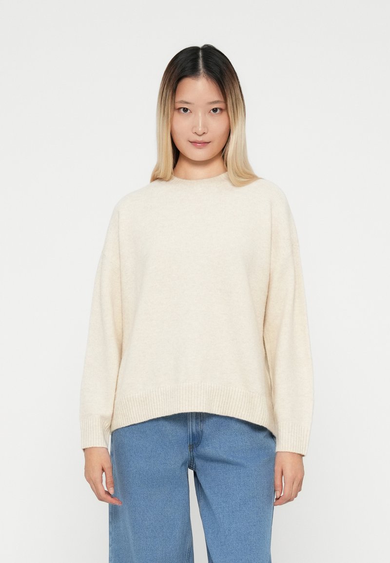 Maglione oversize beige chiaro realizzato in tessuto morbido, con scollatura rotonda e orlo a costine. Abbinato a jeans in denim a gamba larga.