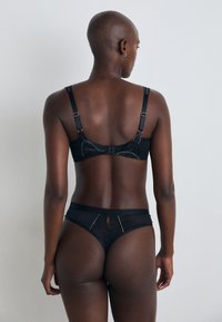 Conjunto de lingerie preto com um soutien com alças ajustáveis e fecho de gancho, combinado com uma anágua alta transparente com detalhes em costura dourada.
