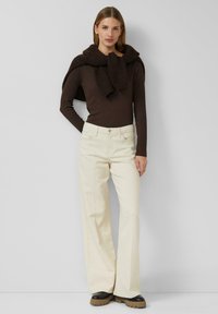 Jasnobeżowe spodnie o szerokich nogawkach z mieszanki bawełny, zestawione z ciemnobrązową bluzką z długim rękawem oraz pasującym dzianinowym szalem zarzuconym na ramiona.