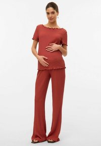 Ensemble en terracotta composé de deux pièces en tissu texturé. Le haut présente un décolleté en dents de scie, tandis que le pantalon est ample et fluide.