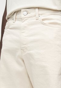 Κοντινή λήψη ανοιχτομπεζ τζιν denim με μεταλλικό κουμπί και ραφές λεπτομέρειες στην μπροστινή τσέπη σε έναν άνθρωπο.