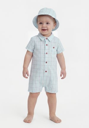 Kleinkind steht barfuß, trägt einen hellblau karierten kurzärmeligen Einteiler und einen passenden Eimerhut, lächelt und schaut nach vorne.