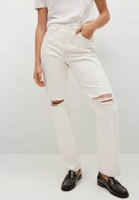 Krémové džíny s vysokým pasem, s dvěma roztrženými koleny a rovnými nohavicemi. Sestavené s černými mokasíny a bílým tričkem.