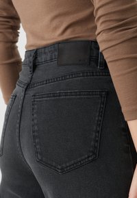 Zwarte denim jeans met een hoge taille, rechte pijpen en een gewoven zwarte leren patch op de achterkant van de tailleband.