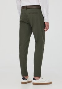 Pantaloni verde oliva slim fit in tessuto texture, con una cintura marrone e due tasche posteriori, abbinati a sneakers bianche.