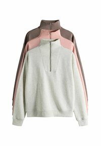 Drei Pullover ausgestellt: hellgrau, rosa und dunkelbraun. Jeder hat einen hohen Kragen mit einem Reißverschluss vorne und einer weichen Textur.