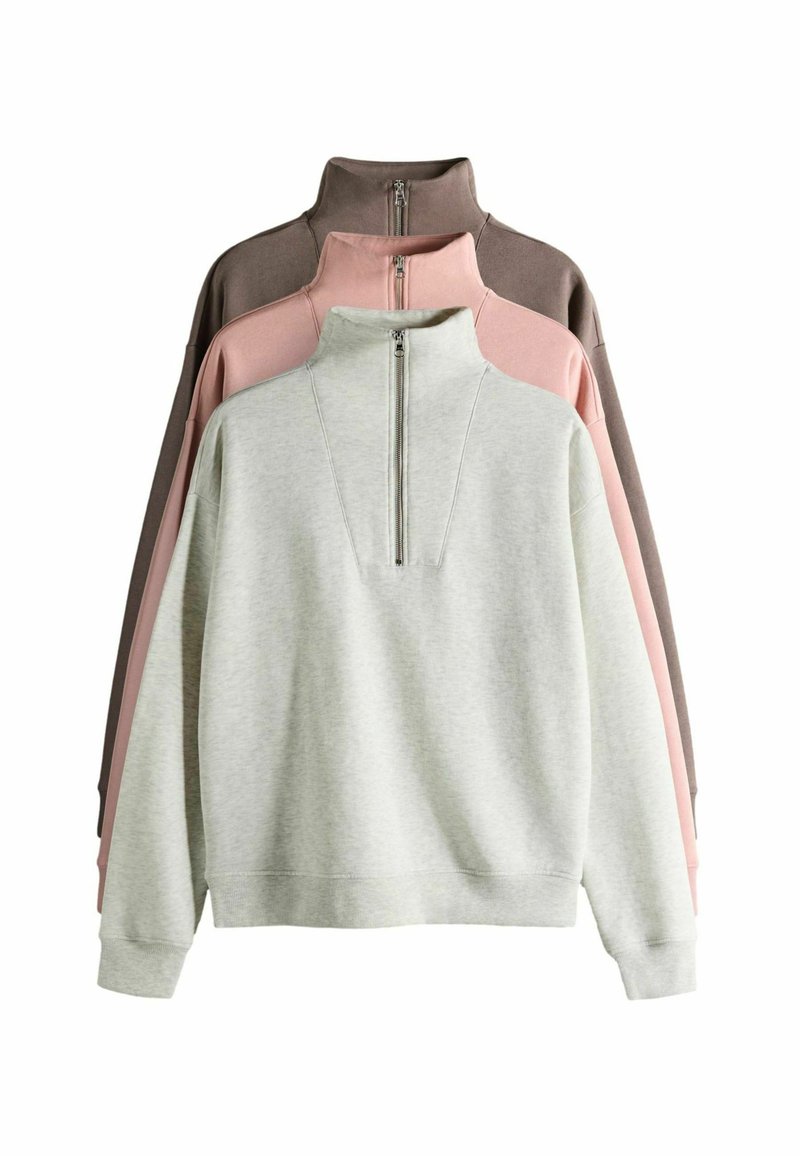 Drei Pullover ausgestellt: hellgrau, rosa und dunkelbraun. Jeder hat einen hohen Kragen mit einem Reißverschluss vorne und einer weichen Textur.