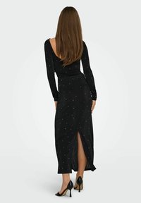 Vestido negro de manga larga con un escote profundo en la espalda, adornado con pequeños acentos en blanco y con una abertura lateral para mayor comodidad al moverse.