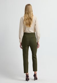 Beige overhemd met lange mouwen gecombineerd met olijfgroene taps toelopende broek. De outfit heeft een eenvoudig ontwerp zonder zichtbare patronen of hardware.