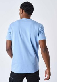 Camiseta de color azul claro con mangas cortas, hecha de algodón. Textura suave, corte clásico. La vista trasera muestra un dobladillo redondeado y detalles de diseño mínimos.