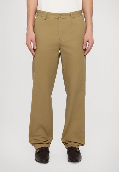 Khaki cotton pants with a relaxed fit, featuring a button closure and belt loops. Worn with dark loafers and a white shirt.