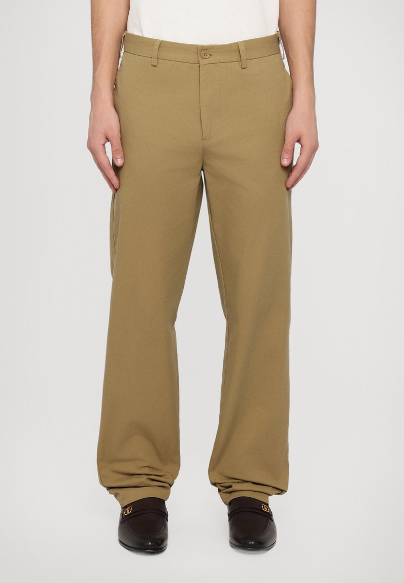 Khaki cotton pants with a relaxed fit, featuring a button closure and belt loops. Worn with dark loafers and a white shirt.
