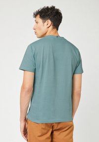 T-shirt a maniche corte teal con collo rotondo e orlo dritto. Materiale in cotone morbido, con un piccolo accentuazione sul retro del collo.