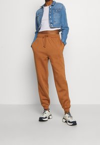 Bruna sweatpants med elastisk midja och mudd, i kombination med en blå denimjacka i cropped stil och vita sneakers med marinblå detaljer.