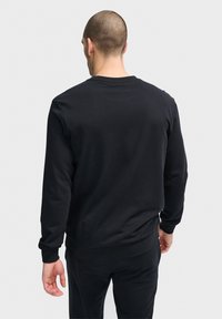 Svart crewneck sweatshirt med långa ärmar, ribbade muddar och nederkant, tillverkad av mjukt tyg med en slät textur, visad bakifrån.