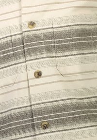 Camicia a maniche corte beige con strisce orizzontali in diverse tonalità di marrone. Presenta due tasche sul petto e chiusure a bottone.