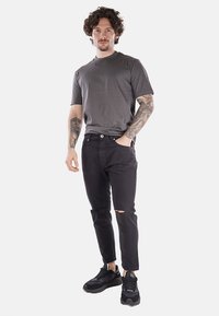 Jeans neri con strappi sulle ginocchia, abbinati a una t-shirt grigia a girocollo. Presentano una vestibilità comoda, tasche e sneakers nere con suola spessa.