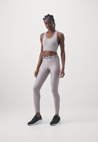 Completo sportivo composto da un reggiseno sportivo grigio chiaro e leggings a vita alta abbinati con un elastico nero "RUNDER", completato da sneakers nere.
