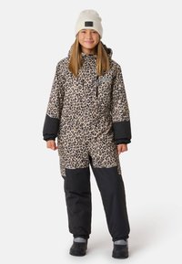 Schneeanzug mit Leopardenmuster in Beige und Schwarz, mit einem Reißverschluss vorne, zwei Seitentaschen und elastischen Bündchen. Kombiniert mit einer cremefarbenen Mütze.