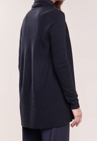 Granatowy sweter z dzianiny z wysokim kołnierzem, długimi rękawami i prążkowaną fakturą u dołu i na mankietach. Posiada lekko oversize'owy krój.