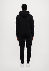 Černá mikina s kapucí a tepláky z měkké látky, s kapucí, žebrovanými manžetami a lemem. Kontrast s bílými teniskami.