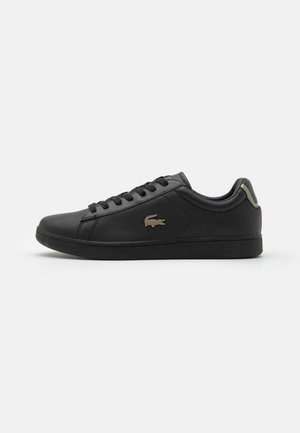 Czarny niski sneaker z wiązaniem, skórzana cholewka i małe beżowe logo krokodyla po boku na białym tle.