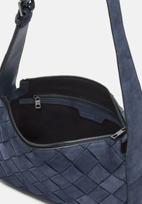 Borsa blu in suede con motivo intrecciato, chiusura con zip e rifiniture in pelle. L'interno presenta una tasca con zip e una morbida fodera nera.