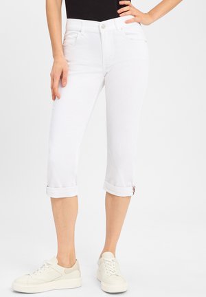Weiße, angeschnittene Jeans mit umgeschlagenem Saum und Fünf-Taschen-Design, aus Denim mit glatter Textur; kombiniert mit weißen Sneakers.