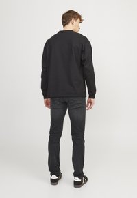 Camisa negra de manga larga con un corte relajado, combinada con jeans oscuros, que muestran una textura suave y un diseño sencillo. Zapatillas completas el look.