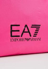 Růžová nylonová taška s černým potiskem loga "EA7 EMPORIO ARMANI." Hladký povrch s čistým designem a výrazným písmem.