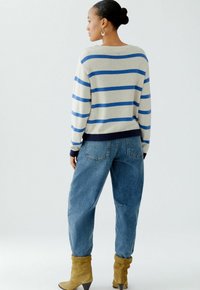 Beige gestreifter Pullover mit blauen horizontalen Streifen und marineblauen Akzenten, kombiniert mit hellblauen weit geschnittenen Jeans und gelben Ankle Boots.