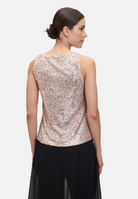 Top na ramiączkach w kolorze różowego złota z cekinami, z okrągłym dekoltem, bez rękawów i gładką teksturą. Noszony z luźną czarną spódnicą.