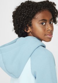 Sudadera con capucha de color azul claro y textura suave, con costuras en contraste y un ajuste relajado, vista de lado y desde atrás.