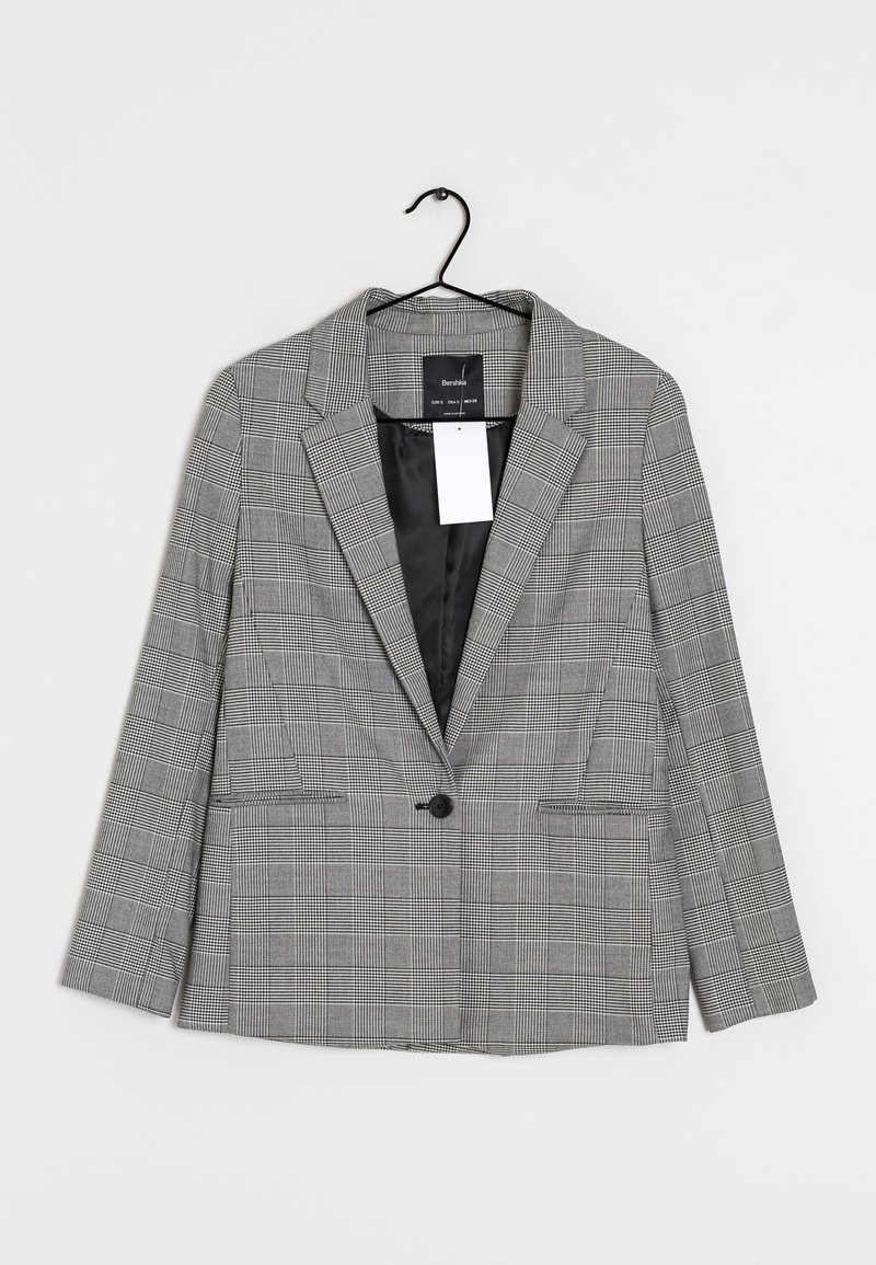Šedý kostkovaný blazer s jednobuttonovým zapínáním, klopami a dvěma předními kapsami, a černou podšívkou. Visí na černém háčku.