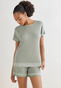 Ljusgrön loungeklädesset bestående av en kortärmad topp och shorts. Båda har vitt spetsdetalj längs fållen och ärmarna. Mjuk textur.