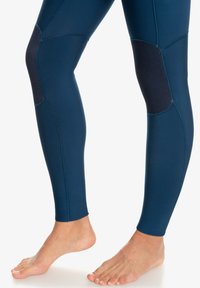 Leggings azul marino fabricados con tejido elástico, que cuentan con parches texturizados en las rodillas, costuras planas y un diseño ajustado.