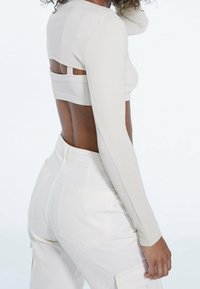Licht geribbelde, crèmekleurige top met lange mouwen en een open rugontwerp, gecombineerd met hooggetailleerde witte cargobroek met zijzakken.