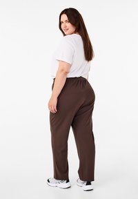Brown trousers with a relaxed fit and elastic waistband, paired with a loose-fitting white t-shirt. Worn with white athletic shoes.