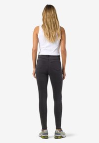 Juodos juosmens aukščio siaurėjančios džinsinės kelnės su ryškiomis siūlėmis, dviem galinėmis kišenėmis ir lygia tekstūra. Dėvimos su balta liemene ir sportbačiais.