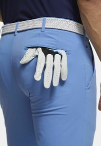 Lichtblauwe golfbroeken met een gestructureerde witte gevlochten riem hebben een zak met een paar witte en zwarte golfhandschoenen.