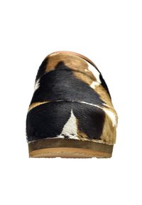 Zoccoli in pelle di mucca con un motivo nero, marrone e bianco, punta arrotondata e suola in legno naturale. Superficie testurizzata con finitura simile ai peli.