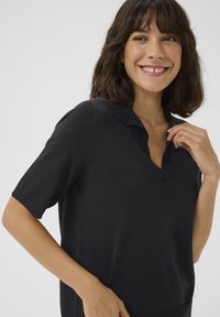 Zwarte polo shirt met korte mouwen en een v-hals, ribgebreide manchetten en een zachte gebreide textuur. Heeft een subtiele kraag en een ontspannen pasvorm.