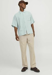 Camisa de botones de manga corta de color azul claro con un bolsillo en el pecho, combinada con pantalones beiges y zapatos oscuros. La camisa tiene un corte relajado.