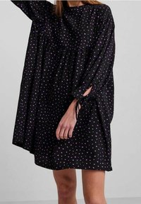 Černé volné šaty s nařaseným designem a drobnými vzory fialových srdíček, dlouhými rukávy a detailem zavazování u manžet.